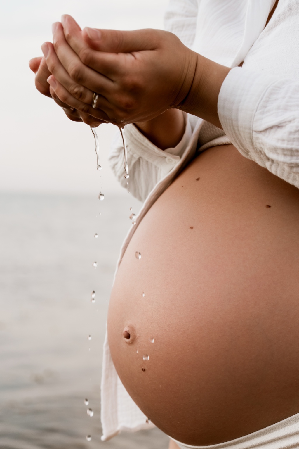 Babybauch mit fallenden Wassertropfen im Detail