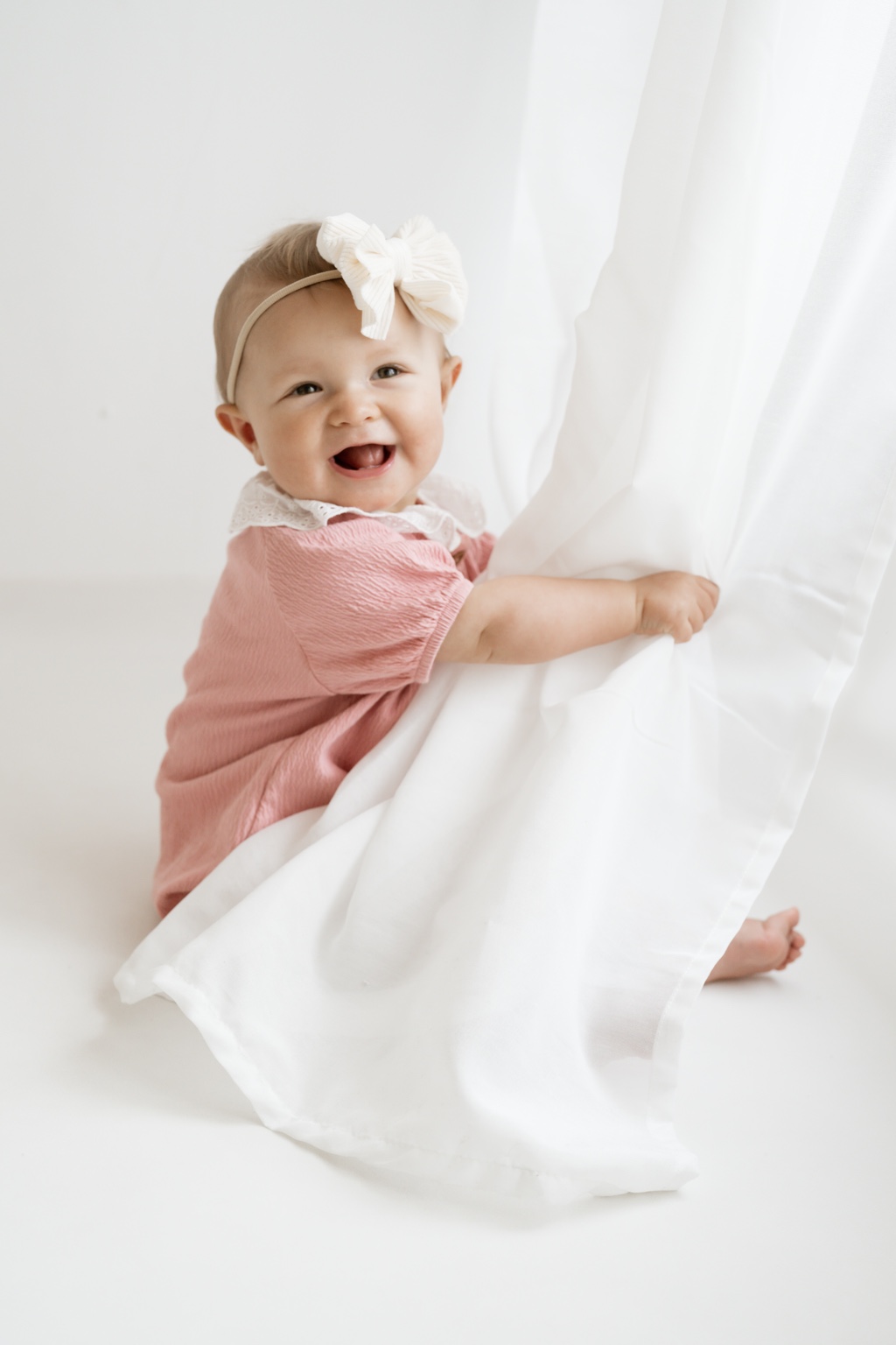 Lachendes Baby spielt am weißen Vorhang